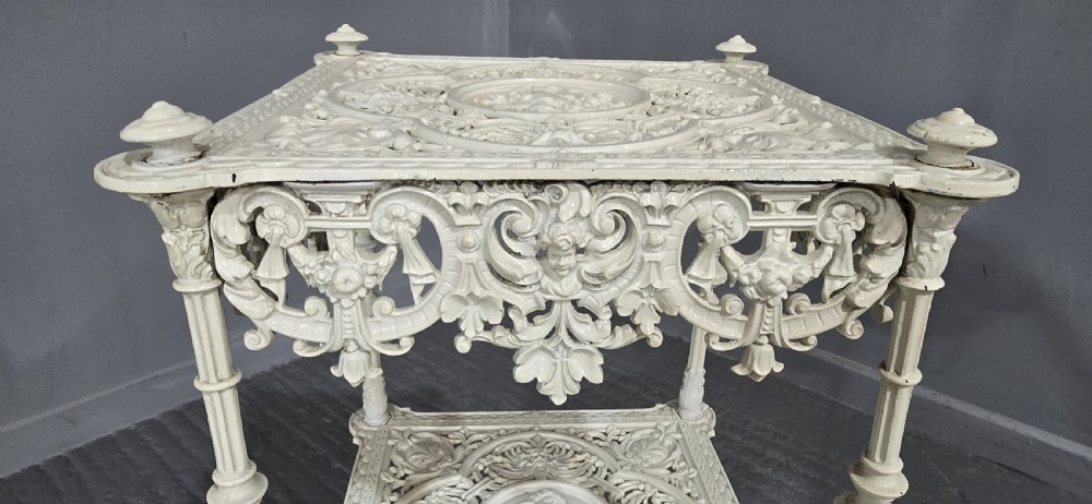 A three-tiered off-white painted cast iron jardiniere stand featuring elaborate openwork scrollwork trays, turned supports, and decorative feet. View V