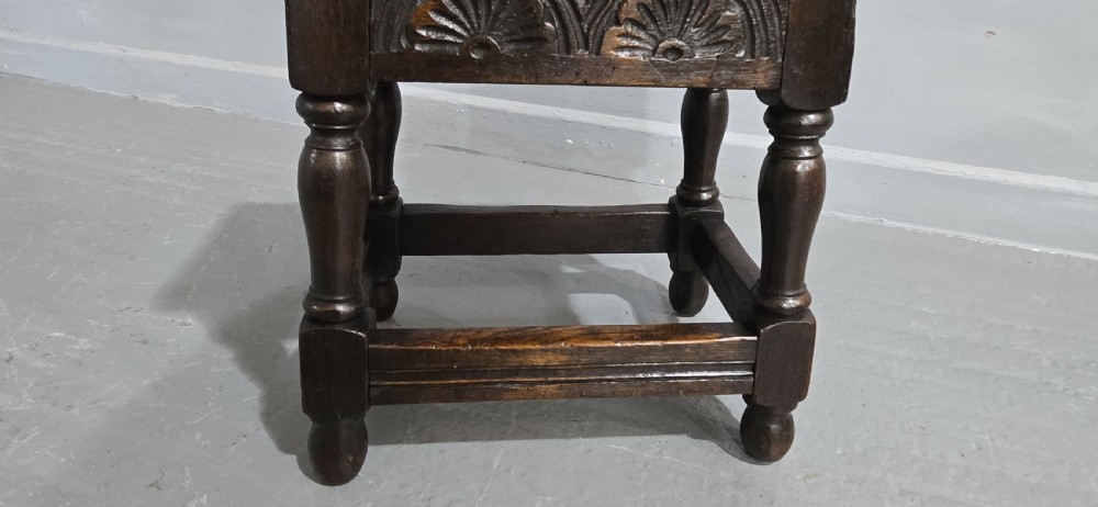A dark oak joint stool featuring carved lunette detail along the frieze, turned legs, and lower wooden stretchers. View IV