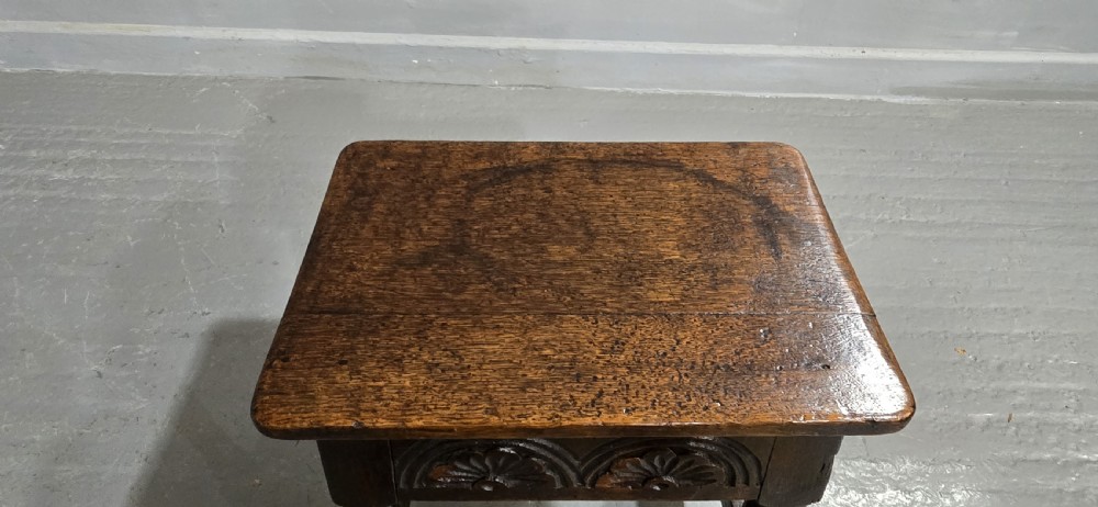 A dark oak joint stool featuring carved lunette detail along the frieze, turned legs, and lower wooden stretchers. View V