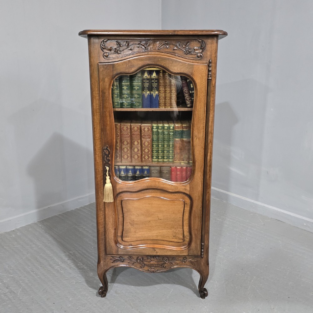 A French walnut single-door bookcase with a carved top frieze, glazed upper panel, solid lower panel, and carved cabriole feet.