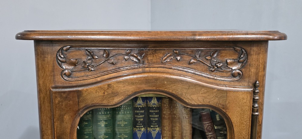 A French walnut single-door bookcase with a carved top frieze, glazed upper panel, solid lower panel, and carved cabriole feet. View II