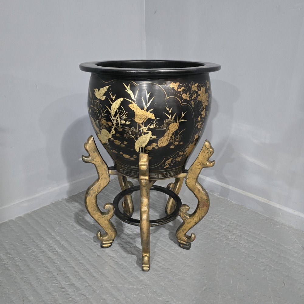 A large black lacquered oriental jardiniere decorated with gold floral and bird imagery, resting upon a carved gold giltwood dragon-form stand.