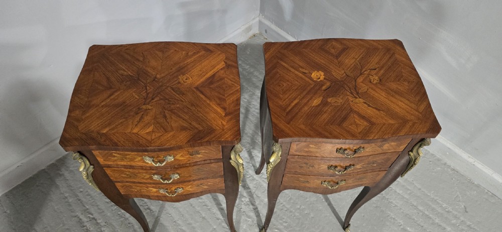 A pair of French Louis XV style bedside tables featuring floral marquetry wood veneers, three drawers, gilt brass mounts, and slender cabriole legs. View VII