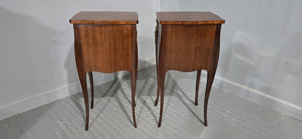 A pair of French Louis XV style bedside tables featuring floral marquetry wood veneers, three drawers, gilt brass mounts, and slender cabriole legs. View X