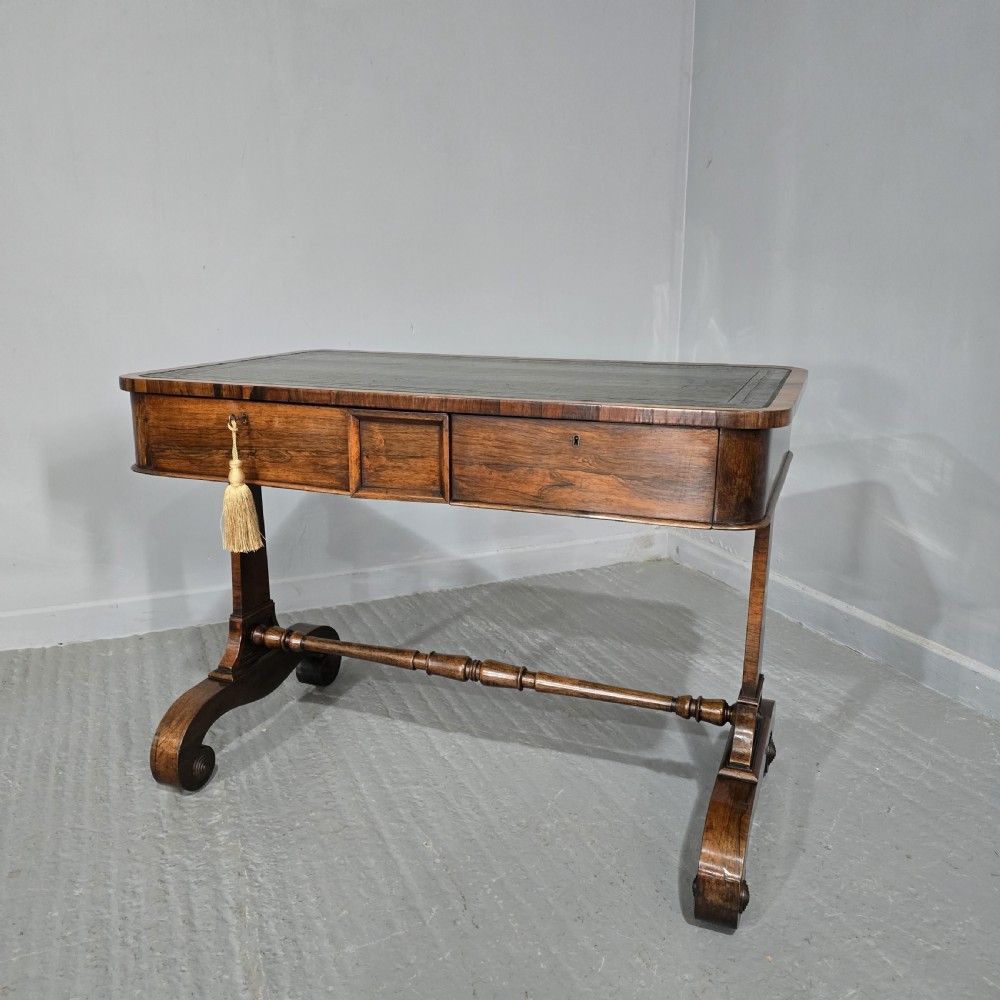 A Regency dark rosewood writing sofa table with a leather-inset top, frieze drawers, scroll feet, and a turned stretcher.