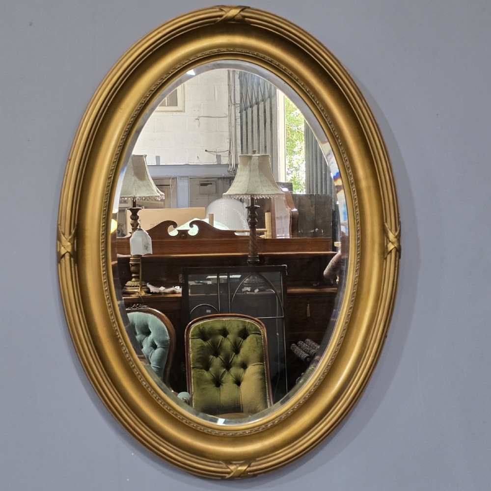 A large Victorian oval wall mirror featuring a ribbed gilt frame with crossed ribbon motifs surrounding a bevelled glass mirror plate. View II