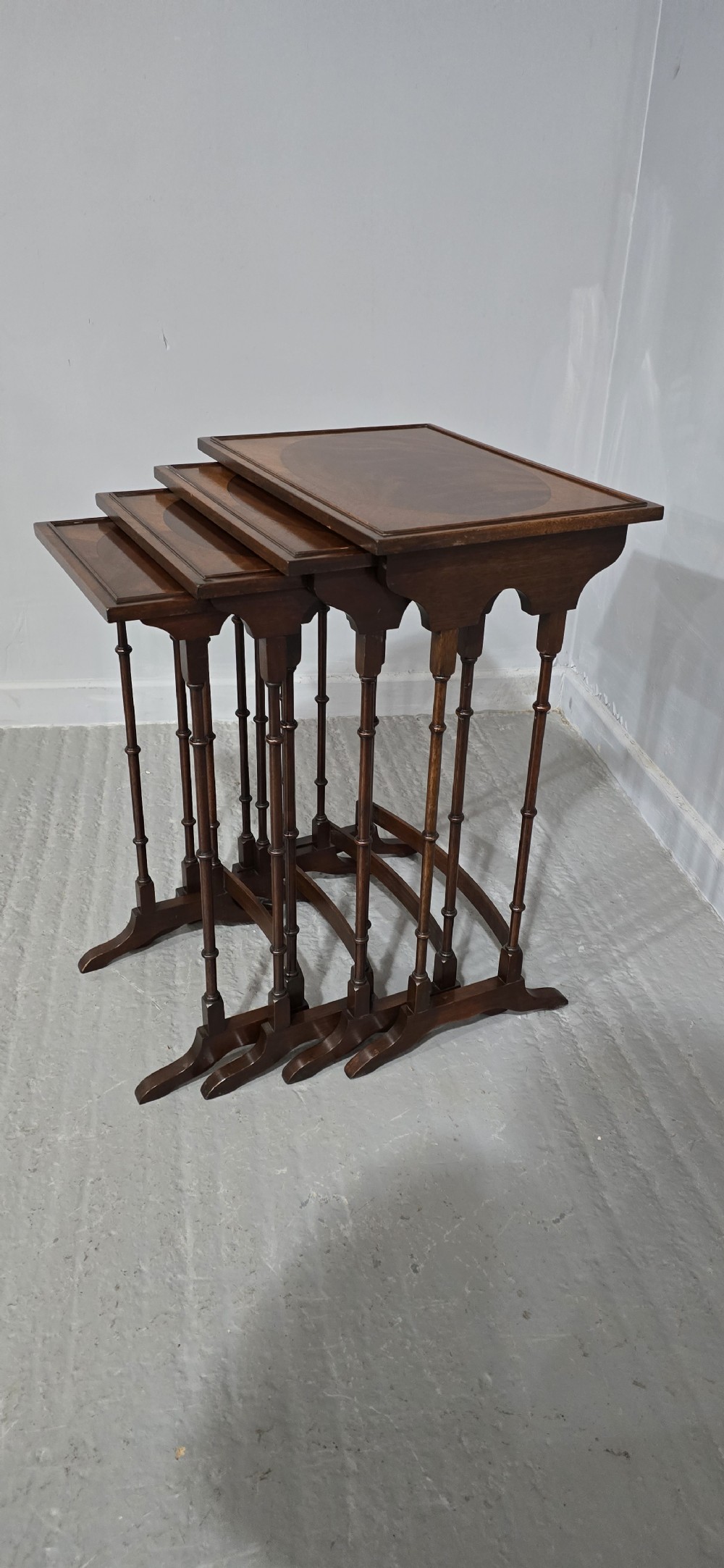 A set of four graduated mahogany quartetto tables featuring oval inlaid tops, ring-turned spindle legs, and curved stretchers. View X