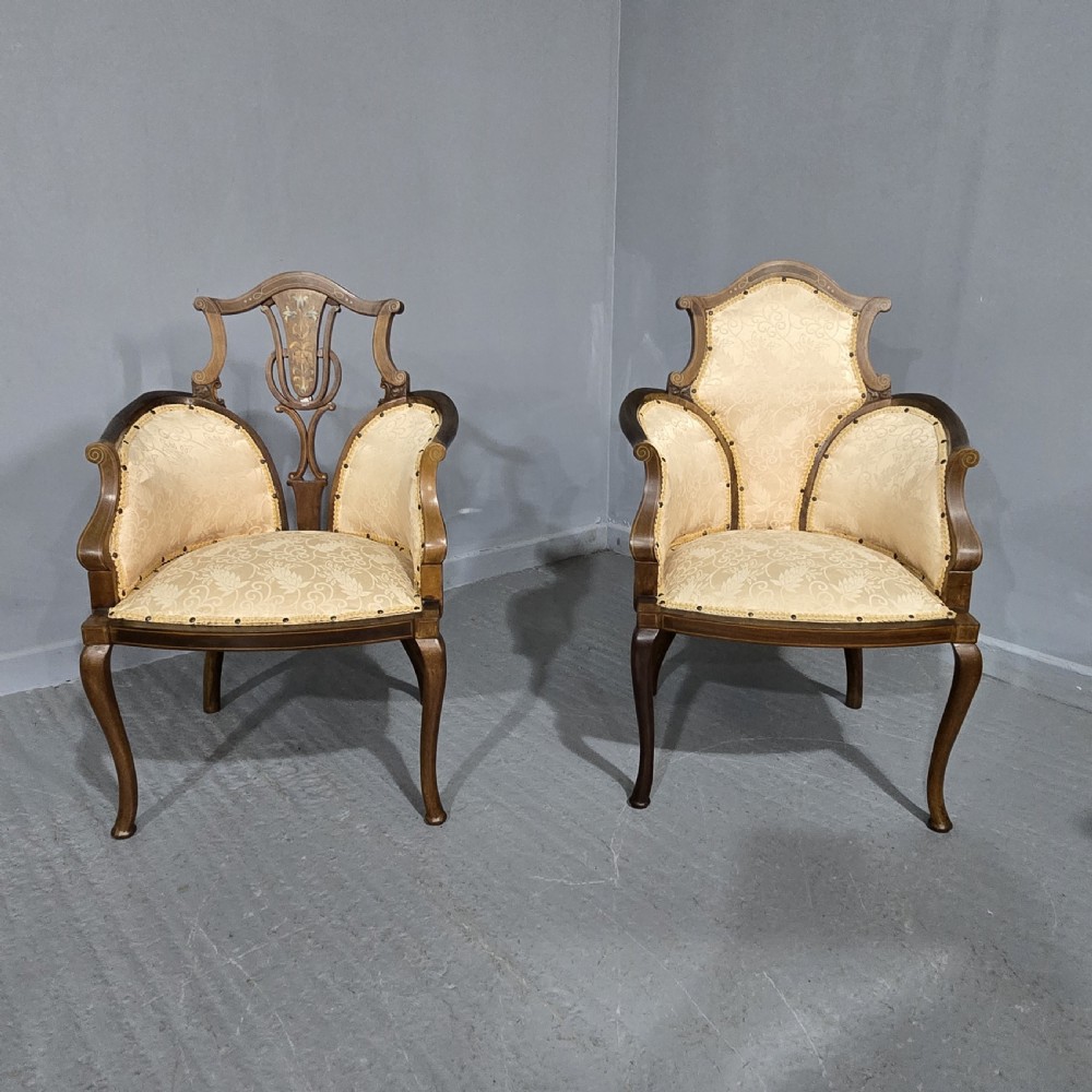 A pair of Edwardian Art Nouveau mahogany armchairs featuring cream floral upholstery, decorative back splats with marquetry inlay, and curved legs.