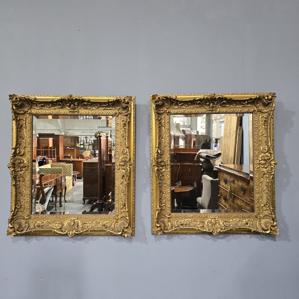 A pair of matching rectangular wall mirrors featuring gold giltwood frames embellished with ornate shell motifs and relief scrollwork.