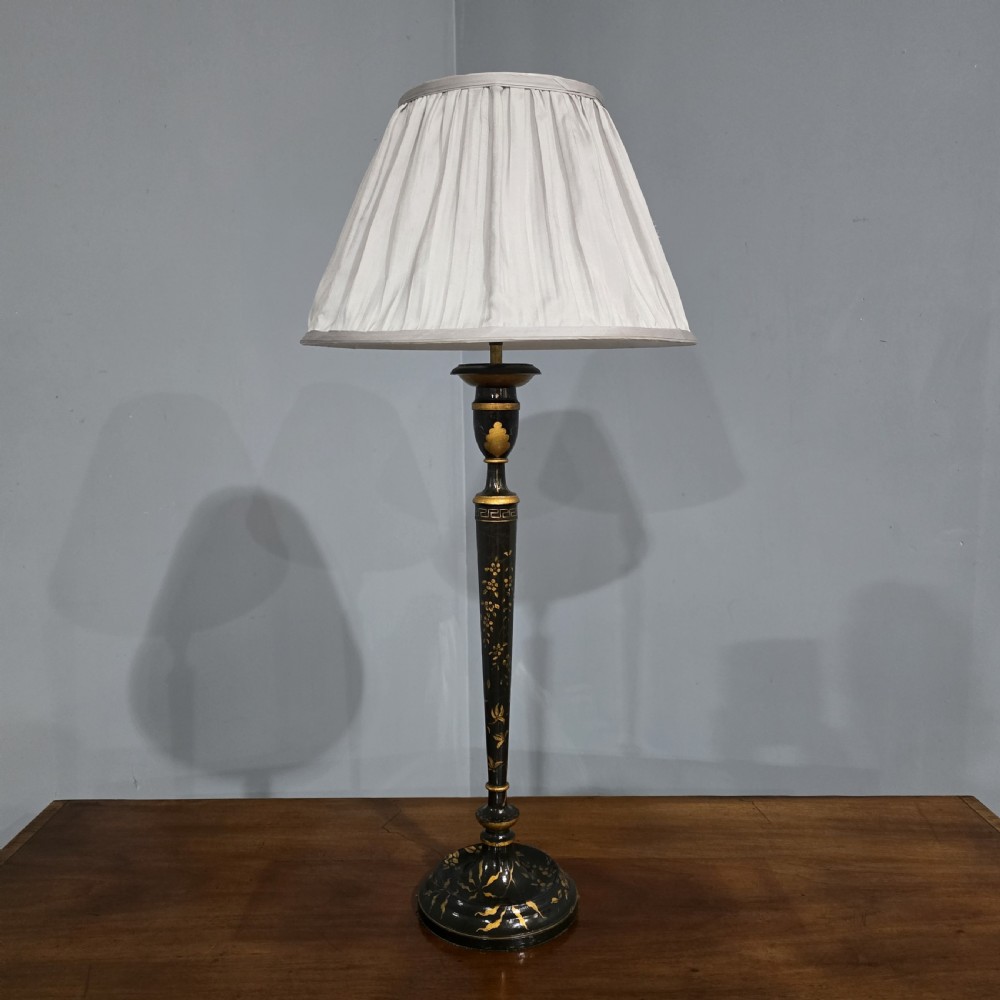 A tall black lacquered table lamp with gilded chinoiserie floral patterns and a pleated light grey fabric shade.