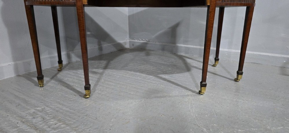 A George III style inlaid mahogany sideboard featuring a central drawer above an arched aperture, flanked by vertical fluted cupboards on tapered legs with brass castors. View III