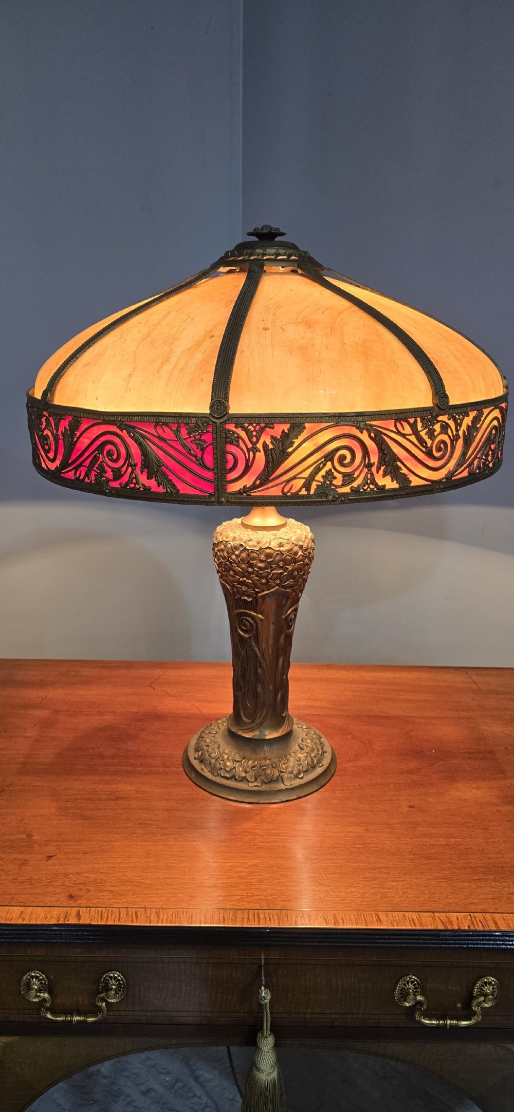 An Art Nouveau table lamp featuring a domed amber and red slag glass shade with decorative metal filigree set on a cast bronze floral base.