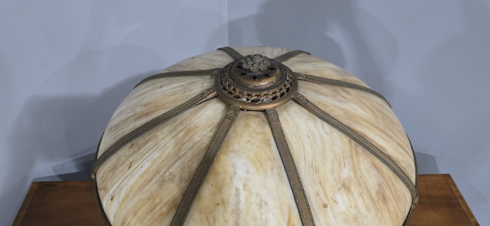 An Art Nouveau table lamp featuring a domed amber and red slag glass shade with decorative metal filigree set on a cast bronze floral base. View V