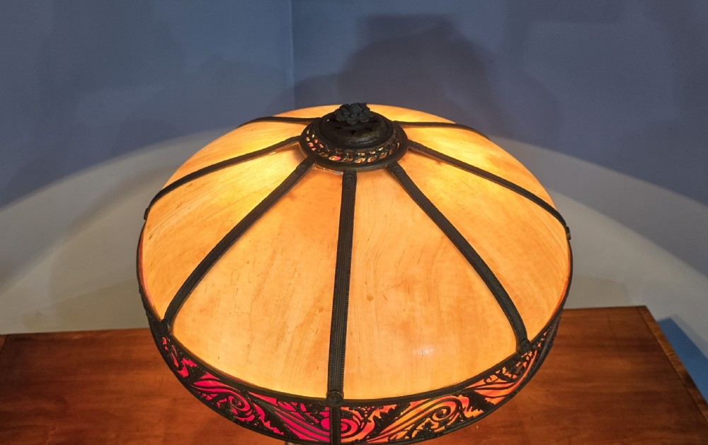 An Art Nouveau table lamp featuring a domed amber and red slag glass shade with decorative metal filigree set on a cast bronze floral base. View VIII