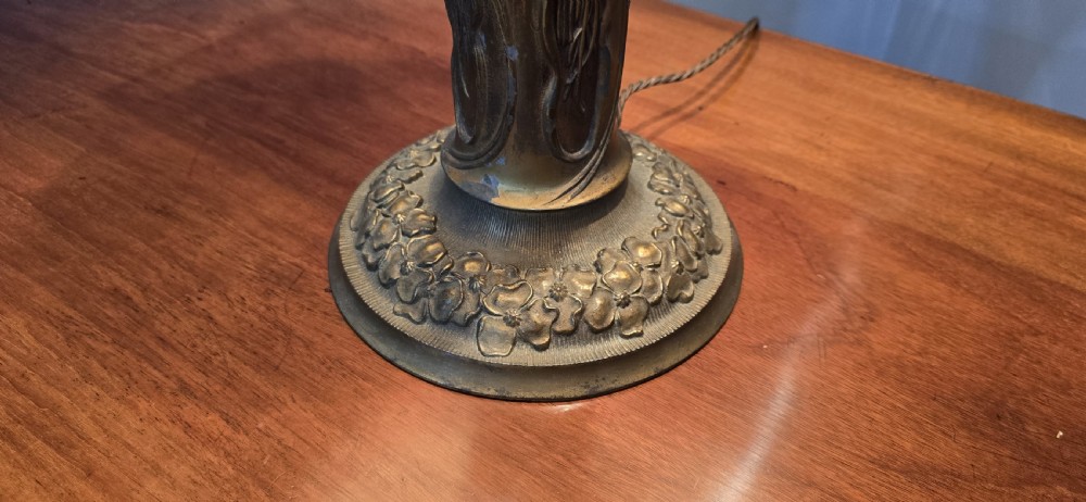 An Art Nouveau table lamp featuring a domed amber and red slag glass shade with decorative metal filigree set on a cast bronze floral base. View XII