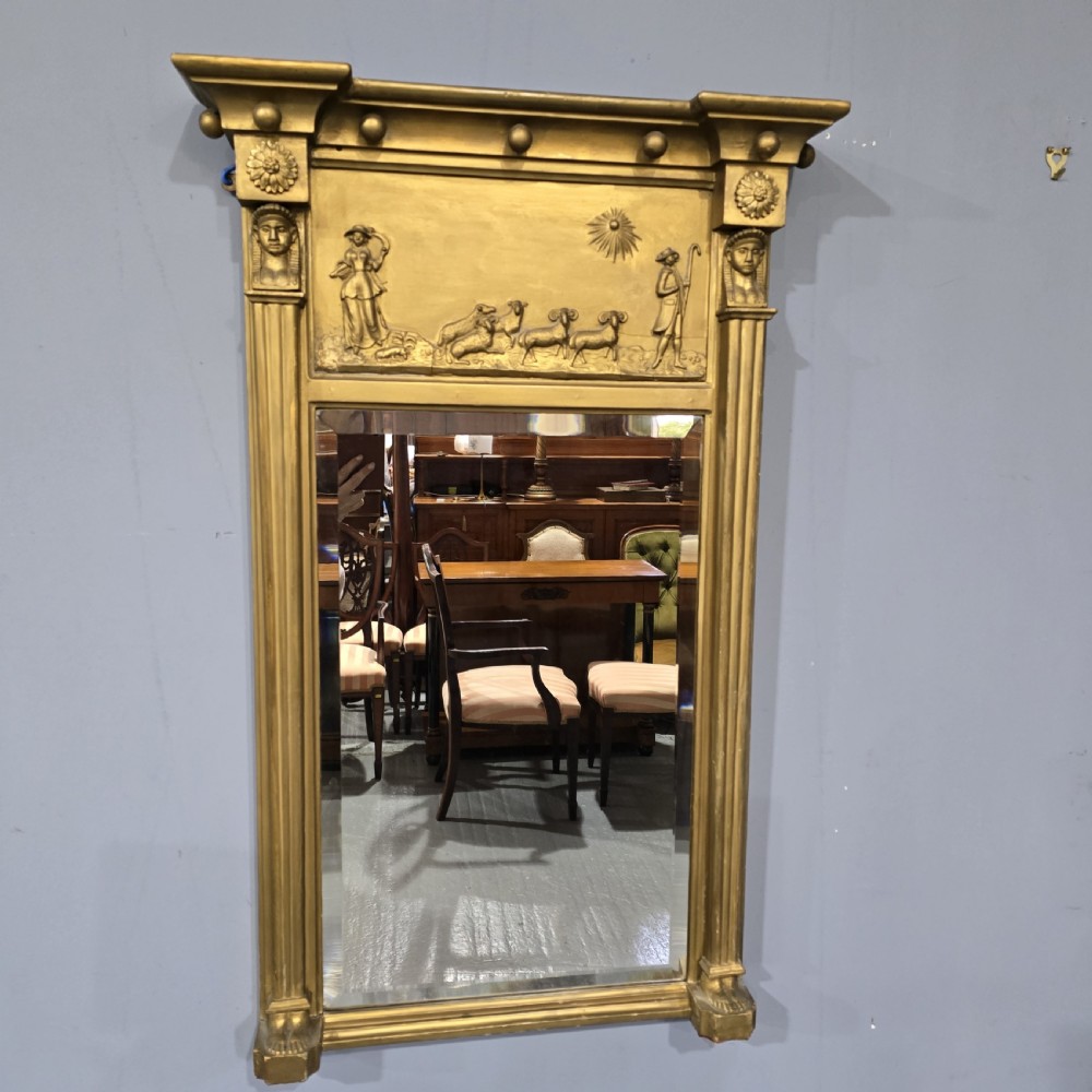 An antique gilded Regency wall mirror featuring an upper bas-relief frieze panel depicting a pastoral scene, fluted pilasters, and ball ornamentation along the upper cornice.