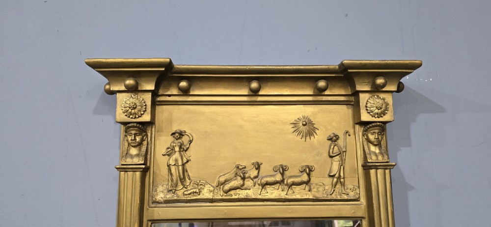 An antique gilded Regency wall mirror featuring an upper bas-relief frieze panel depicting a pastoral scene, fluted pilasters, and ball ornamentation along the upper cornice. View III