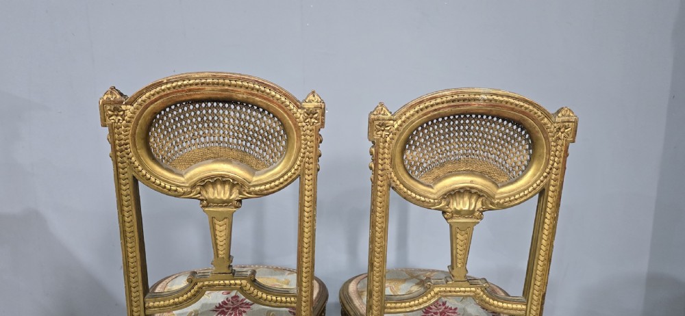 A pair of gold giltwood Louis XVI style side chairs featuring oval cane backs, carved splats, fluted legs, and patterned seat upholstery. View V