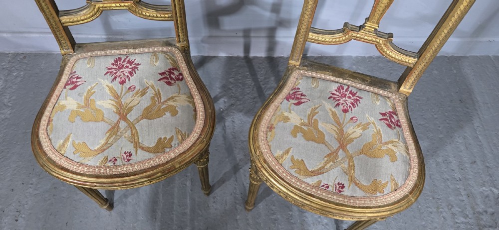 A pair of gold giltwood Louis XVI style side chairs featuring oval cane backs, carved splats, fluted legs, and patterned seat upholstery. View VI