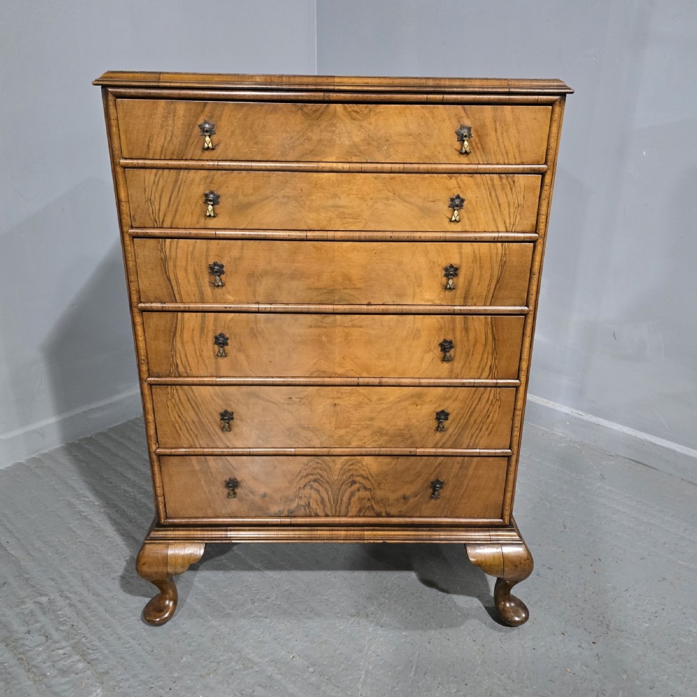 A tall antique burr walnut chest of drawers featuring six graduated drawers with brass drop handles and cabriole legs.