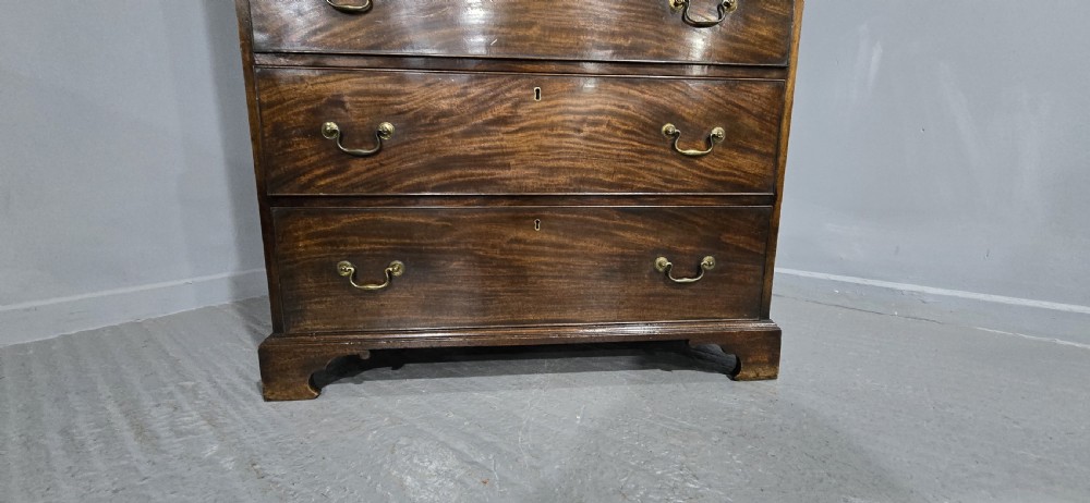 A tall Georgian mahogany chest on chest featuring two stacked drawer sections, flame mahogany grain, dentil cornice moulding, brass swan-neck handles, and bracket feet. View VI