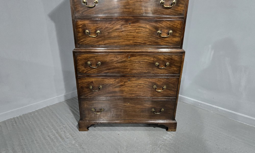 A tall Georgian mahogany chest on chest featuring two stacked drawer sections, flame mahogany grain, dentil cornice moulding, brass swan-neck handles, and bracket feet. View XII