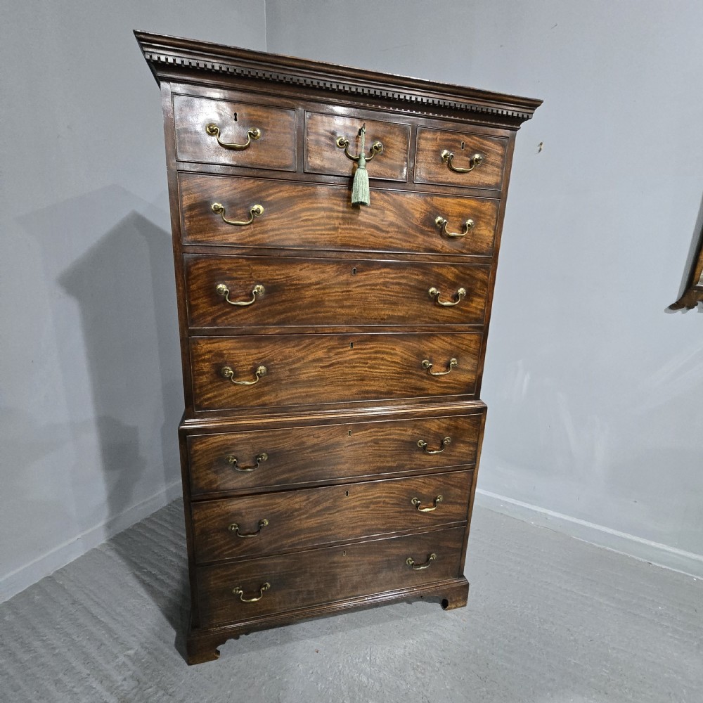 A tall Georgian mahogany chest on chest featuring two stacked drawer sections, flame mahogany grain, dentil cornice moulding, brass swan-neck handles, and bracket feet. View XIV