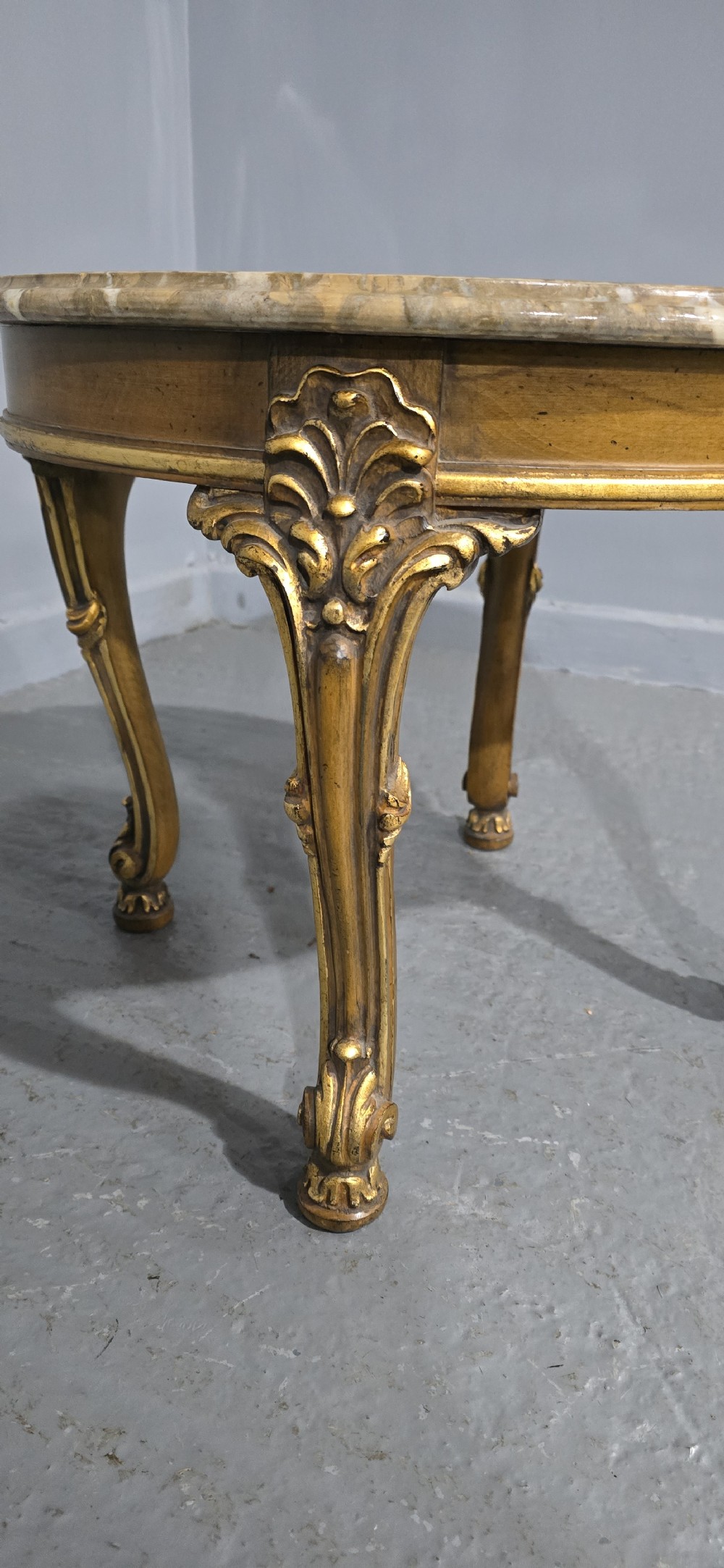A circular French style low coffee table with a polished beige marble top and carved giltwood cabriole legs. View III