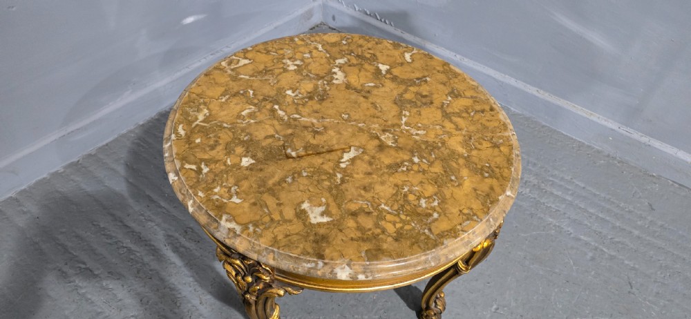 A circular French style low coffee table with a polished beige marble top and carved giltwood cabriole legs. View V