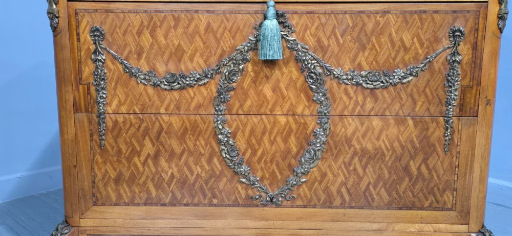 A French satinwood commode chest featuring herringbone parquetry veneer, a variegated marble top, and decorative gilt-bronze mounts. View III