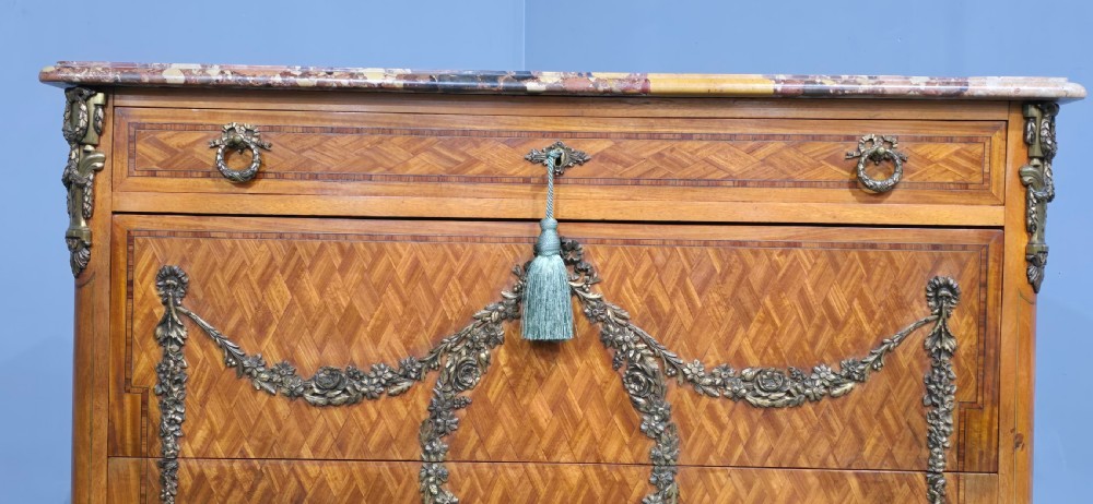 A French satinwood commode chest featuring herringbone parquetry veneer, a variegated marble top, and decorative gilt-bronze mounts. View V