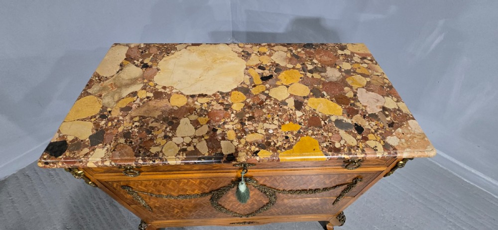 A French satinwood commode chest featuring herringbone parquetry veneer, a variegated marble top, and decorative gilt-bronze mounts. View IX