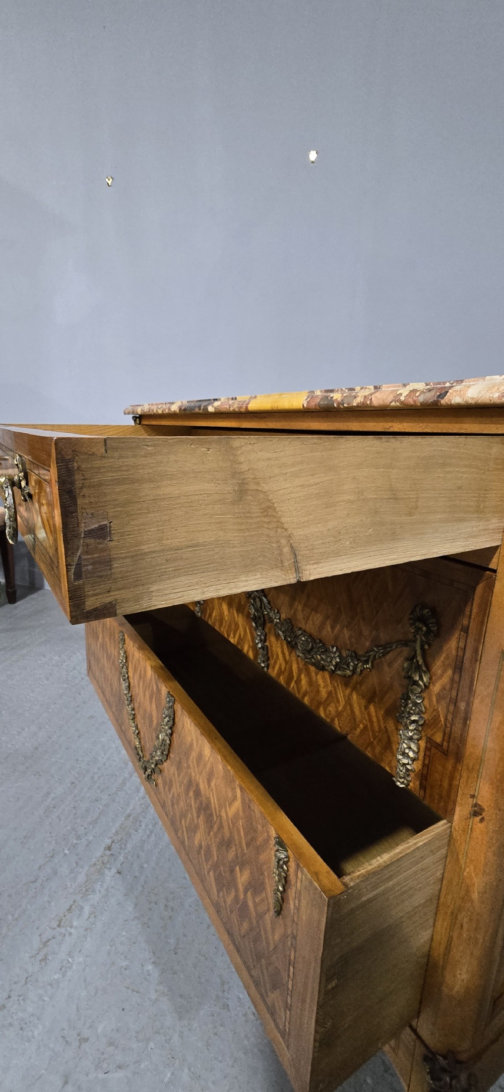 A French satinwood commode chest featuring herringbone parquetry veneer, a variegated marble top, and decorative gilt-bronze mounts. View XIII