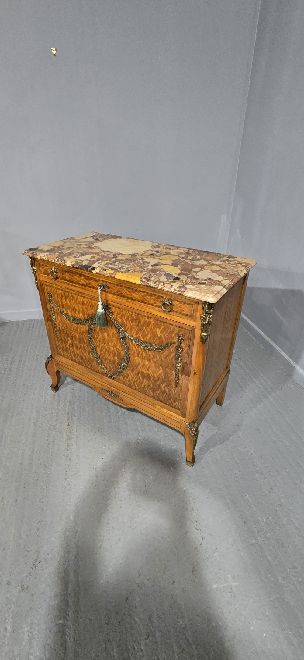 A French satinwood commode chest featuring herringbone parquetry veneer, a variegated marble top, and decorative gilt-bronze mounts. View XIV