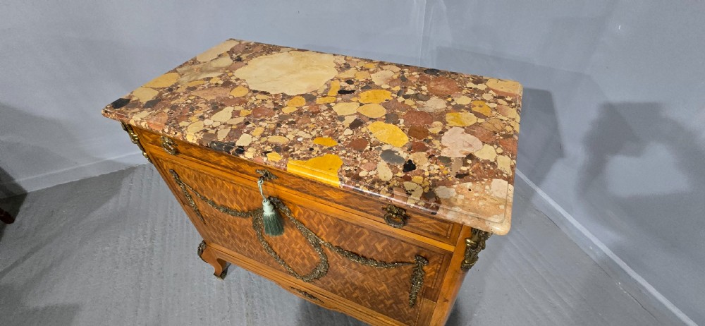 A French satinwood commode chest featuring herringbone parquetry veneer, a variegated marble top, and decorative gilt-bronze mounts. View XV