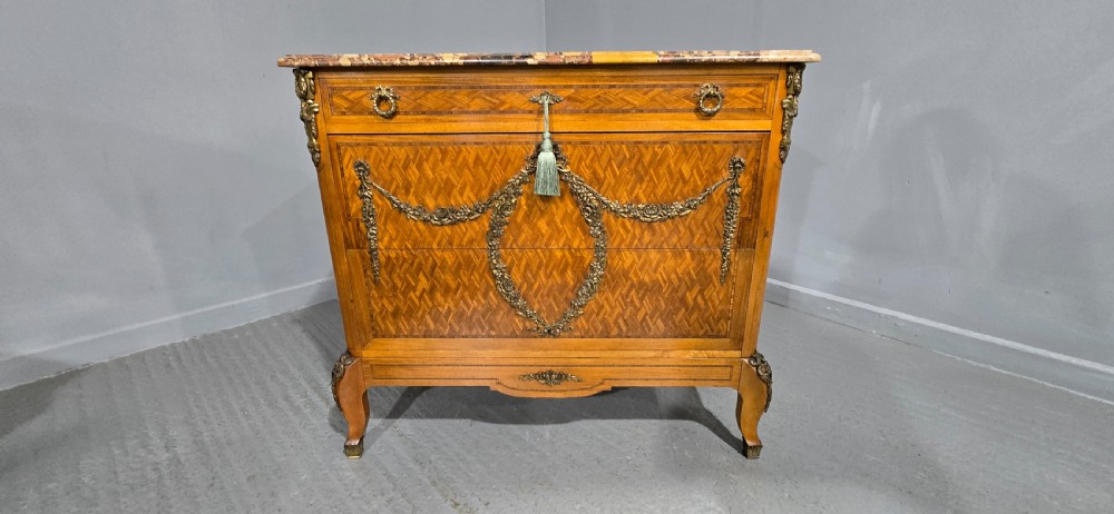 A French satinwood commode chest featuring herringbone parquetry veneer, a variegated marble top, and decorative gilt-bronze mounts. View XVII
