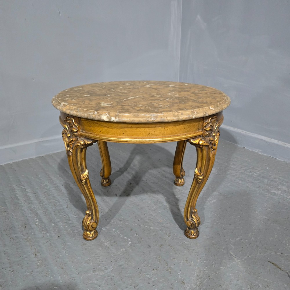 A circular French style low coffee table with a polished beige marble top and carved giltwood cabriole legs.