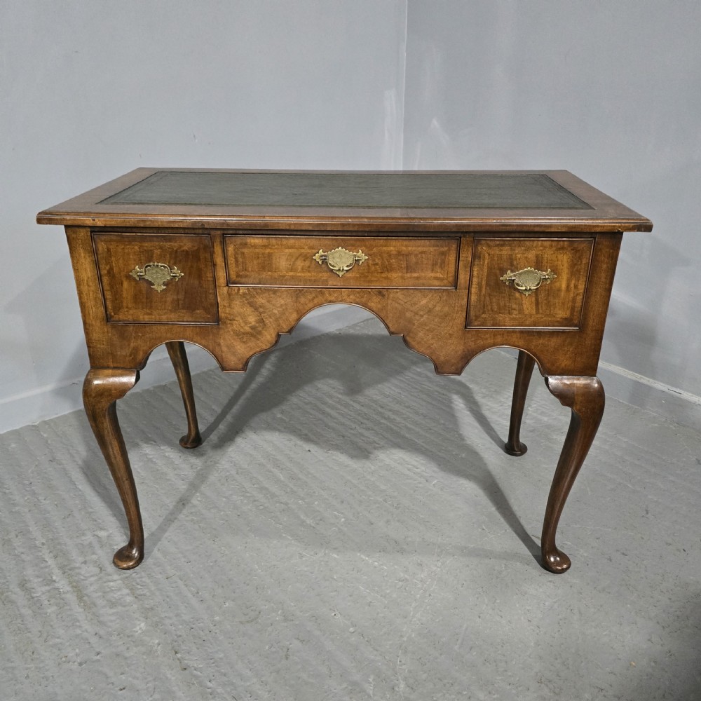 An antique Queen Anne style burr walnut lowboy featuring three drawers, an inset green leather writing top, brass handles, and slender cabriole legs.
