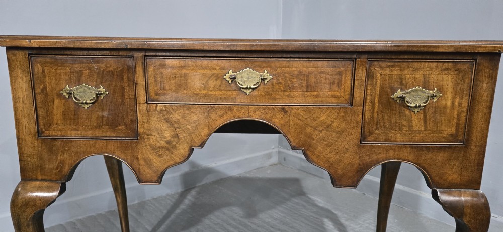 An antique Queen Anne style burr walnut lowboy featuring three drawers, an inset green leather writing top, brass handles, and slender cabriole legs. View III