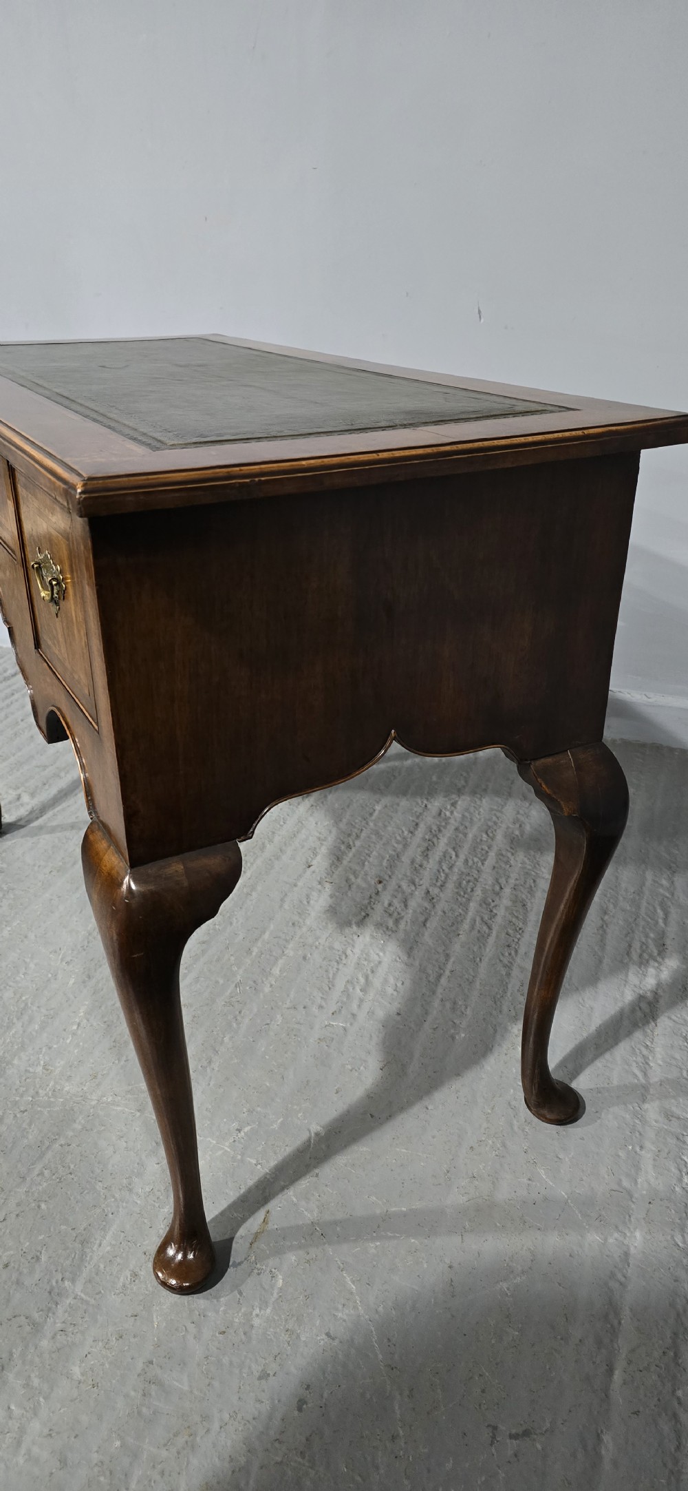 An antique Queen Anne style burr walnut lowboy featuring three drawers, an inset green leather writing top, brass handles, and slender cabriole legs. View VII