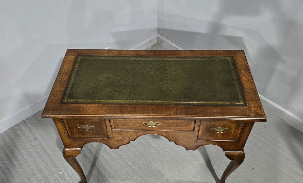 An antique Queen Anne style burr walnut lowboy featuring three drawers, an inset green leather writing top, brass handles, and slender cabriole legs. View X