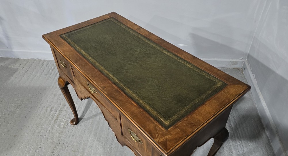 An antique Queen Anne style burr walnut lowboy featuring three drawers, an inset green leather writing top, brass handles, and slender cabriole legs. View XI