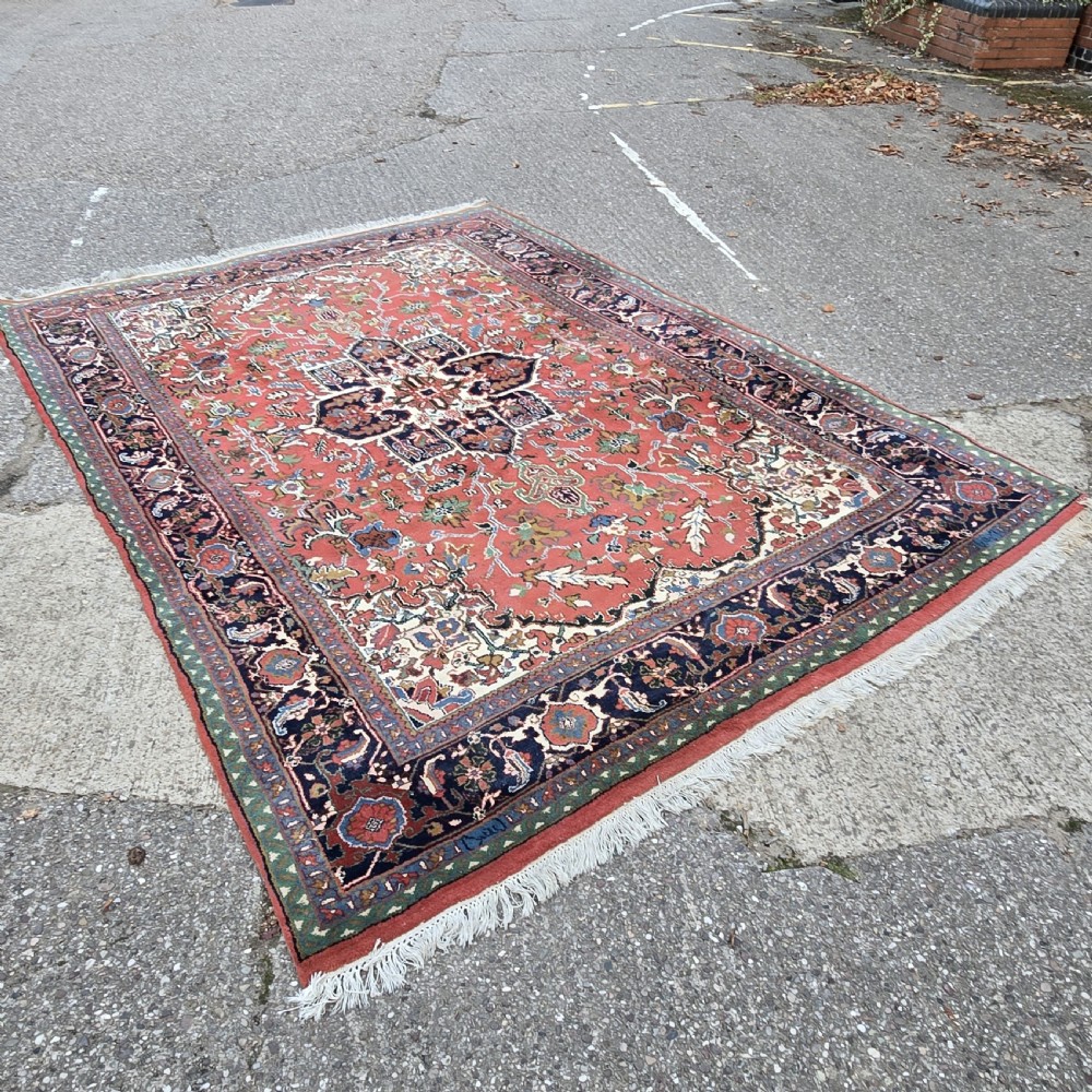 A hand-knotted wool area carpet featuring a large geometric star medallion on a terracotta field with dark navy floral borders and cream fringes.
