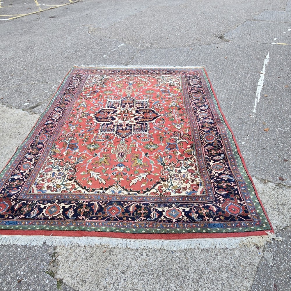 A hand-knotted wool area carpet featuring a large geometric star medallion on a terracotta field with dark navy floral borders and cream fringes. View II