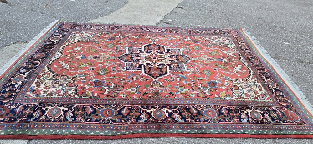 A hand-knotted wool area carpet featuring a large geometric star medallion on a terracotta field with dark navy floral borders and cream fringes. View III