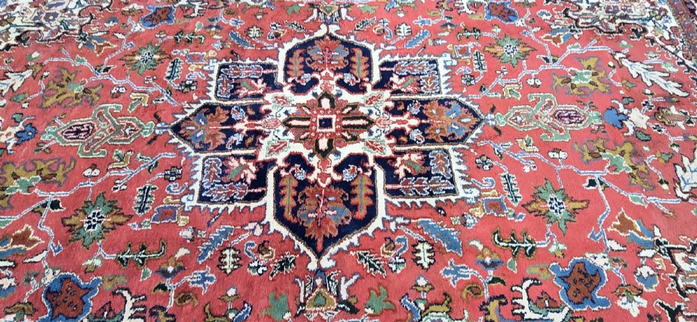 A hand-knotted wool area carpet featuring a large geometric star medallion on a terracotta field with dark navy floral borders and cream fringes. View V