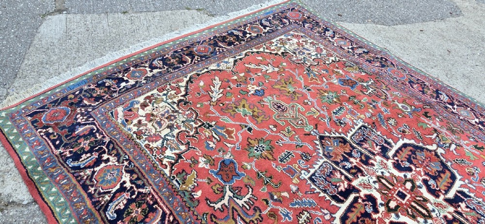 A hand-knotted wool area carpet featuring a large geometric star medallion on a terracotta field with dark navy floral borders and cream fringes. View VI