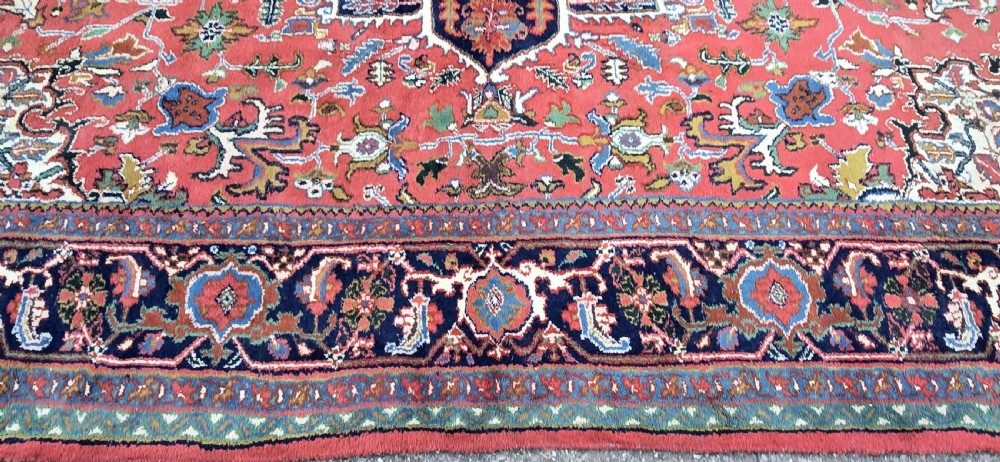 A hand-knotted wool area carpet featuring a large geometric star medallion on a terracotta field with dark navy floral borders and cream fringes. View VII