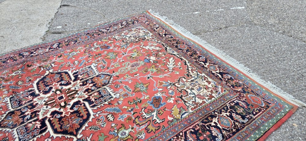 A hand-knotted wool area carpet featuring a large geometric star medallion on a terracotta field with dark navy floral borders and cream fringes. View IX