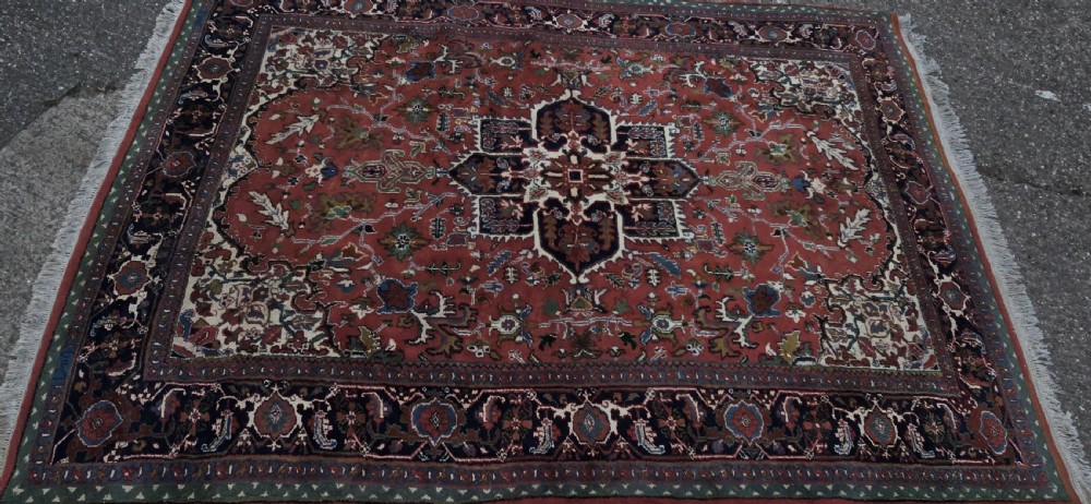 A hand-knotted wool area carpet featuring a large geometric star medallion on a terracotta field with dark navy floral borders and cream fringes. View X